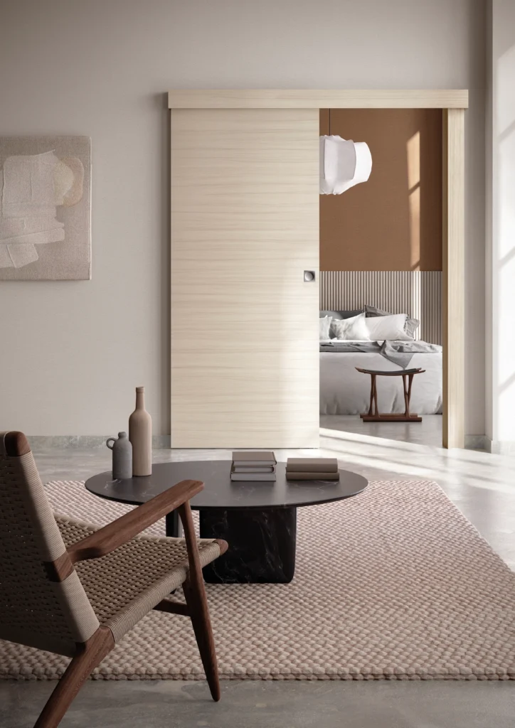 Porta della collezione Zero scorrevole esterno muro con mantovana, in laminato Palissandro Bianco. La porta divide uno spazio salotto da una camera matrimoniale, l'ambiente è neutro e raffinato